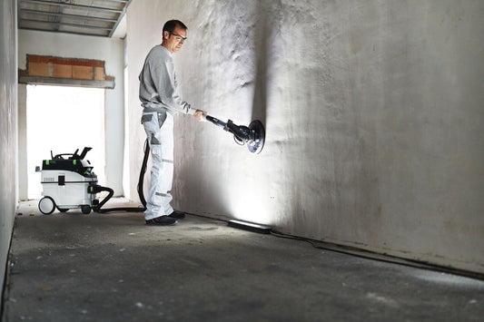Festool Streiflicht SYSLITE STL 450 bei Oberflächenkontrolle an Betonwand, Arbeiter prüft Unebenheiten mit LED-Streiflicht.