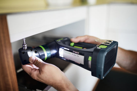 Festool C 18-Basic Akku-Bohrschrauber mit CENTROTEC Schnellwechselsystem in Hand, Akku und Ladegerät sichtbar.
