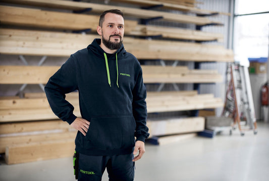 Festool Kapuzenpullover HO-FT2 Unisex-Hoodie in dunkelblau mit grünen Details, getragen in Werkstatt-Umgebung
