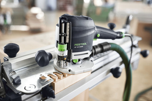 Festool OF 1010 REBQ-FS Oberfräse auf Führungsschiene mit Fräsbox und Zubehör auf Werkbench montiert.