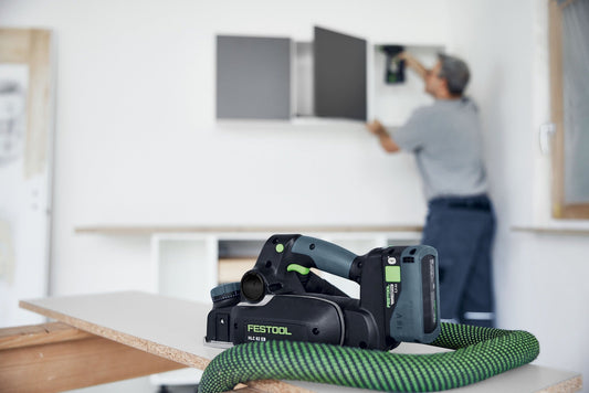 Festool HighPower Akkupack BP 18 Li 5,0 HP-ASI mit grünem Softgrip-Rahmen auf Holzoberfläche, im Hintergrund Anwendung an