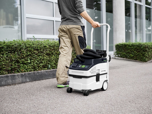 Festool CLEANTEC CT 15 Absaugmobil mit 15-Liter-Behälter in Anwendung auf Gehweg neben Hecke, Mann bedient Transportgriff