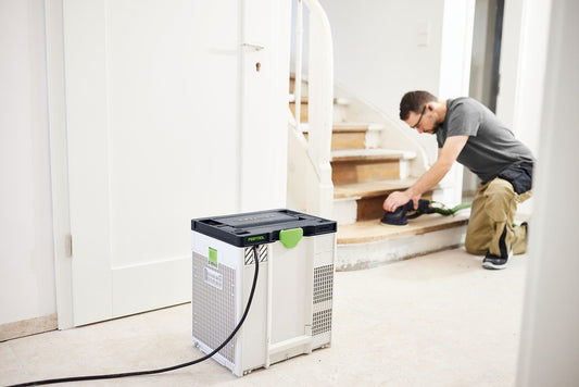 Festool SYS-AIR H Luftreiniger im Einsatz auf Baustelle, Handwerker arbeitet an Treppe, mobiler Luftreiniger im Vordergrund