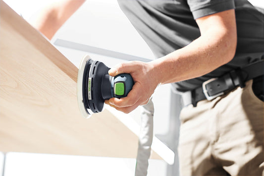 Festool ETS EC 150/5 EQ-Plus Exzenterschleifer in Anwendung auf Holzoberfläche mit grünem Schaltknopf