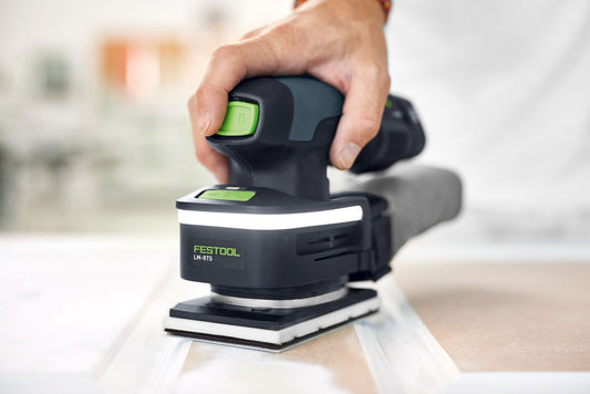 Festool Lichtmodul LM-RTS mit grünem Ein-Aus-Schalter in Hand, montiert auf Kompaktschleifer beim Schleifen von Holz