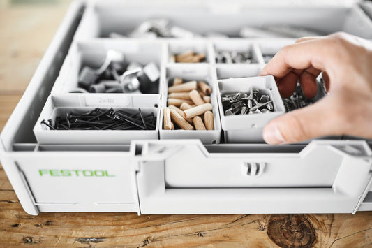Festool Einsatzboxen Box mit sortierten Kleinteilen wie Nägeln, Dübeln und Schrauben in weißen Kunststoffboxen, Hand greift