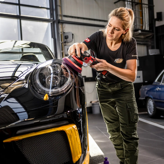 Frau poliert glänzenden schwarzen Sportwagen mit kabelloser FLEX Exzenter-Poliermaschine in moderner Werkstatt – professionelle Autopflege & KFZ-Aufbereitung